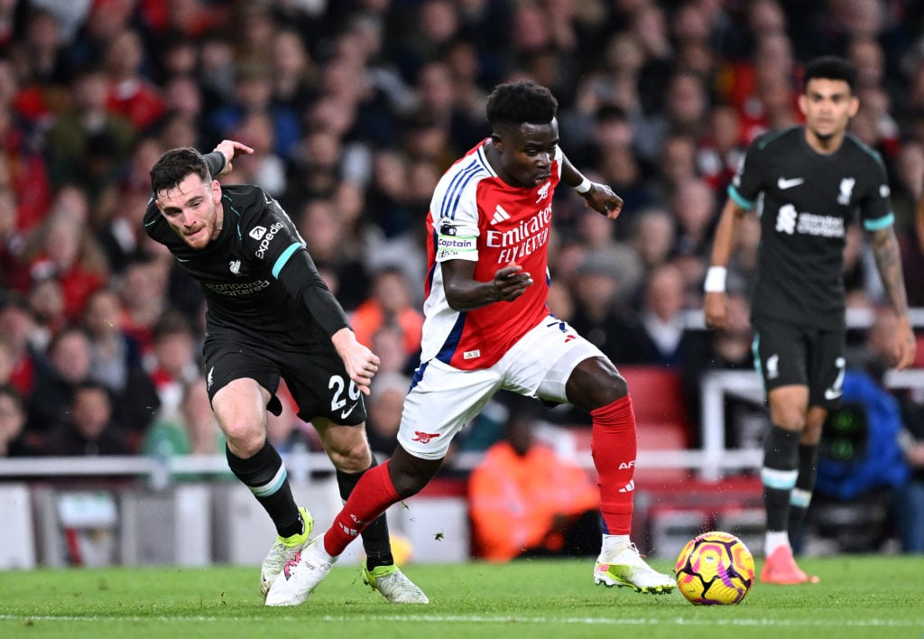 Bukayo Saka of Arsenal runs with the ball whilst under pressure from Andrew Robertson of Liverpool during the Premier League match between Arsenal ...