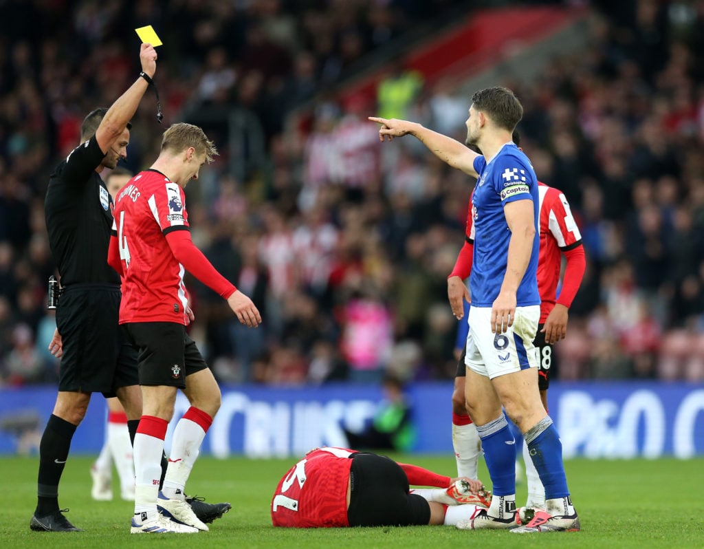 Referee Andy Madley shows a yellow card to James Tarkowski of Everton, as Cameron Archer of Southampton reacts on the floor during the Premier Leag...