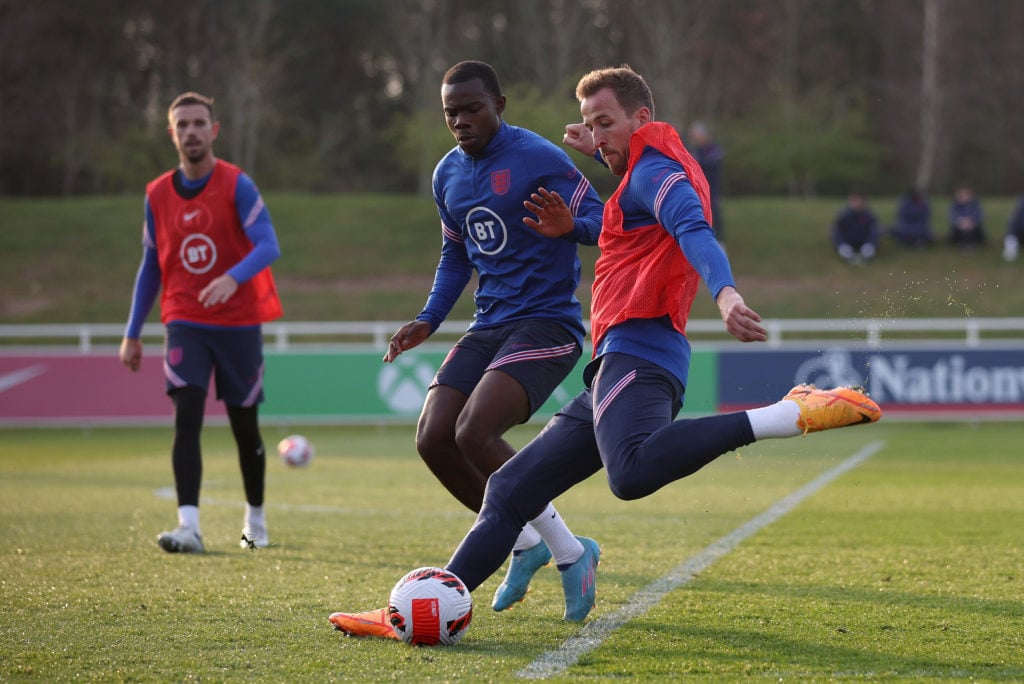 Harry Kane of England shoots under pressure from teammate Tyrick Mitchell during a training session at St Georges Park on March 22, 2022 in Burton-...