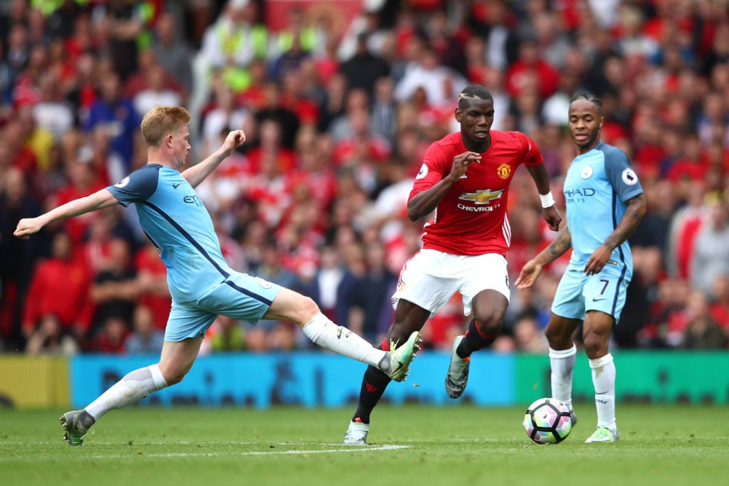 Paul Pogba of Manchester United (C) takes the ball past Kevin De Bruyne of Manchester City (L) during the Premier League match between Manchester U...