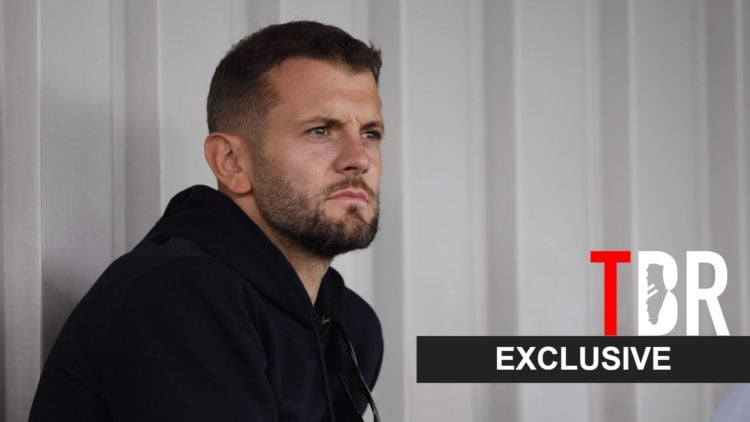 Jack Wilshere looks on during an Arsenal match alongside a TBR Exclusive banner